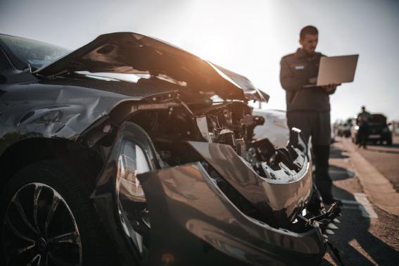 Mechanic working on laptop in front of damaged car